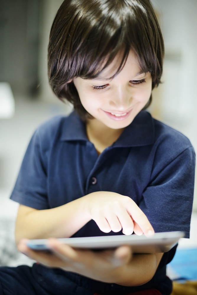 Cute little boy playing with tablet pc in dark room at home